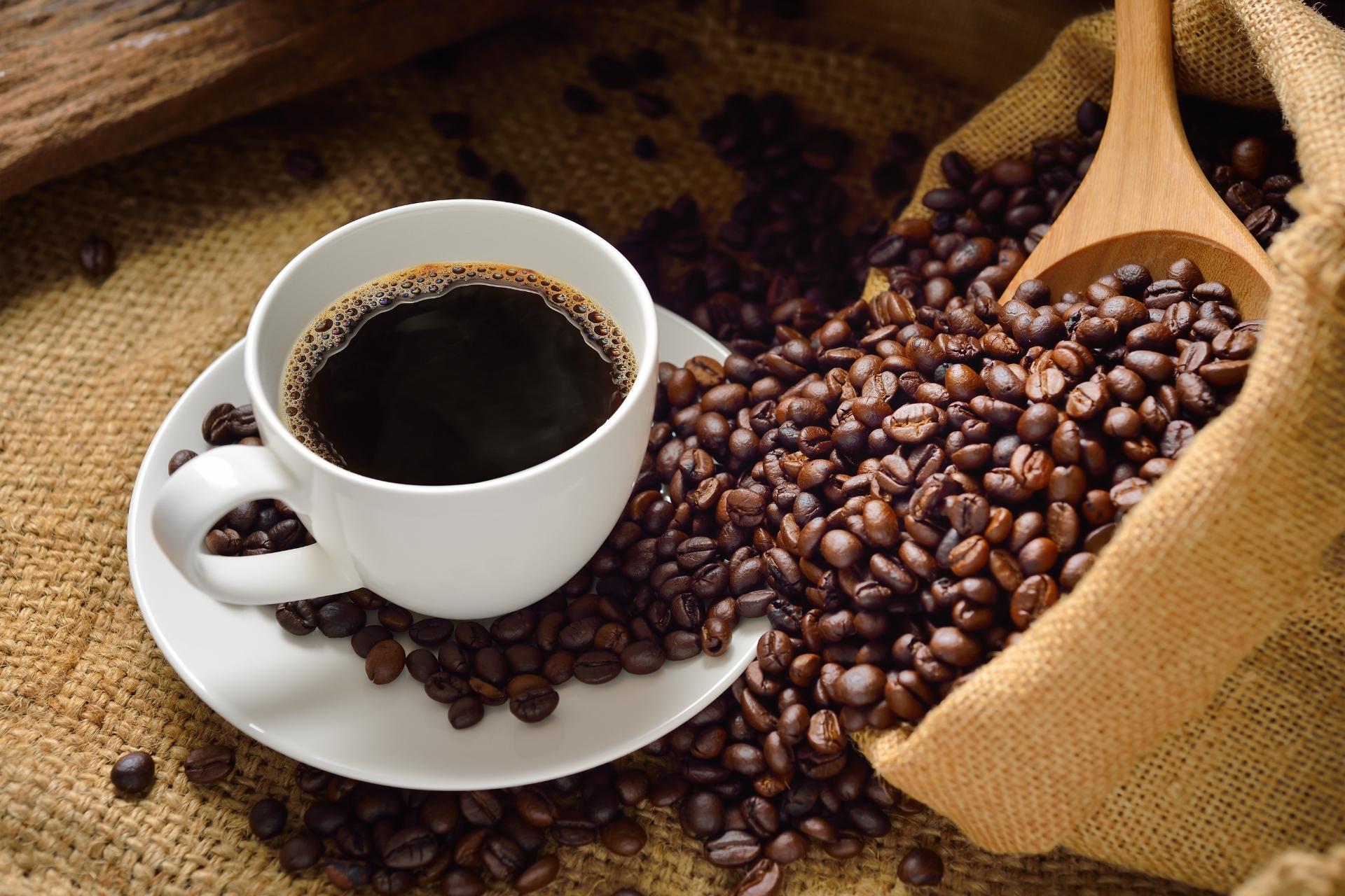 Freshly roasted Ethiopian single-origin specialty coffee beans spilling from a burlap sack with a wooden scoop and a brewed cup of coffee